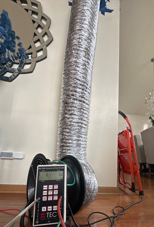 Duct blaster sealed to a floor register with pressure gauge displaying live readings