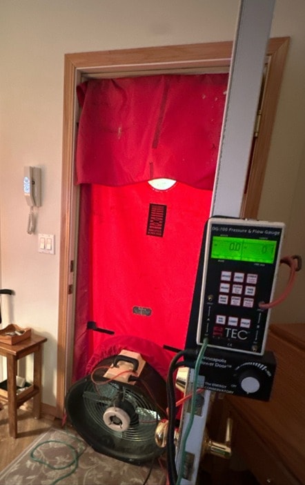 Blower door installed in a doorway with pressure gauge ready to test